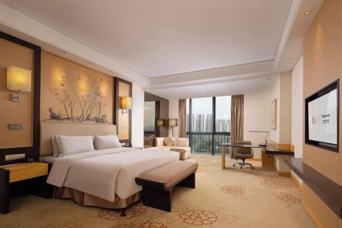 A hotel room with a large bed, a desk, a chair, a sofa, and a TV.