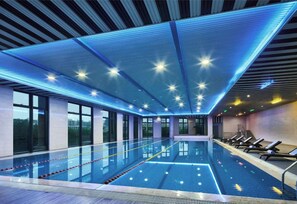 Une piscine intérieure avec des couloirs bien délimités, un plafond doté d’un éclairage bleu et de grandes fenêtres laissant entrer la lumière du soleil.