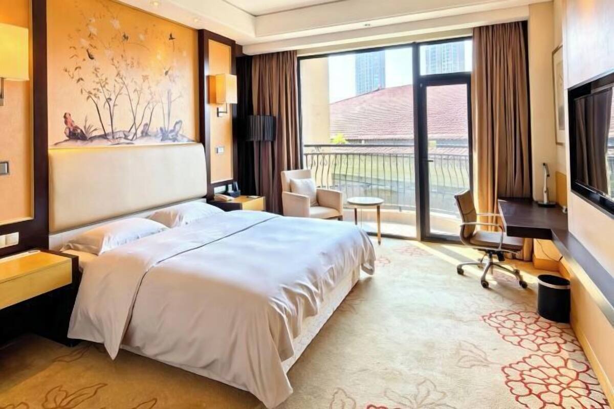 Hotelkamer met een groot bed, een bureau, een stoel, een kleine tafel en een balkon met uitzicht.