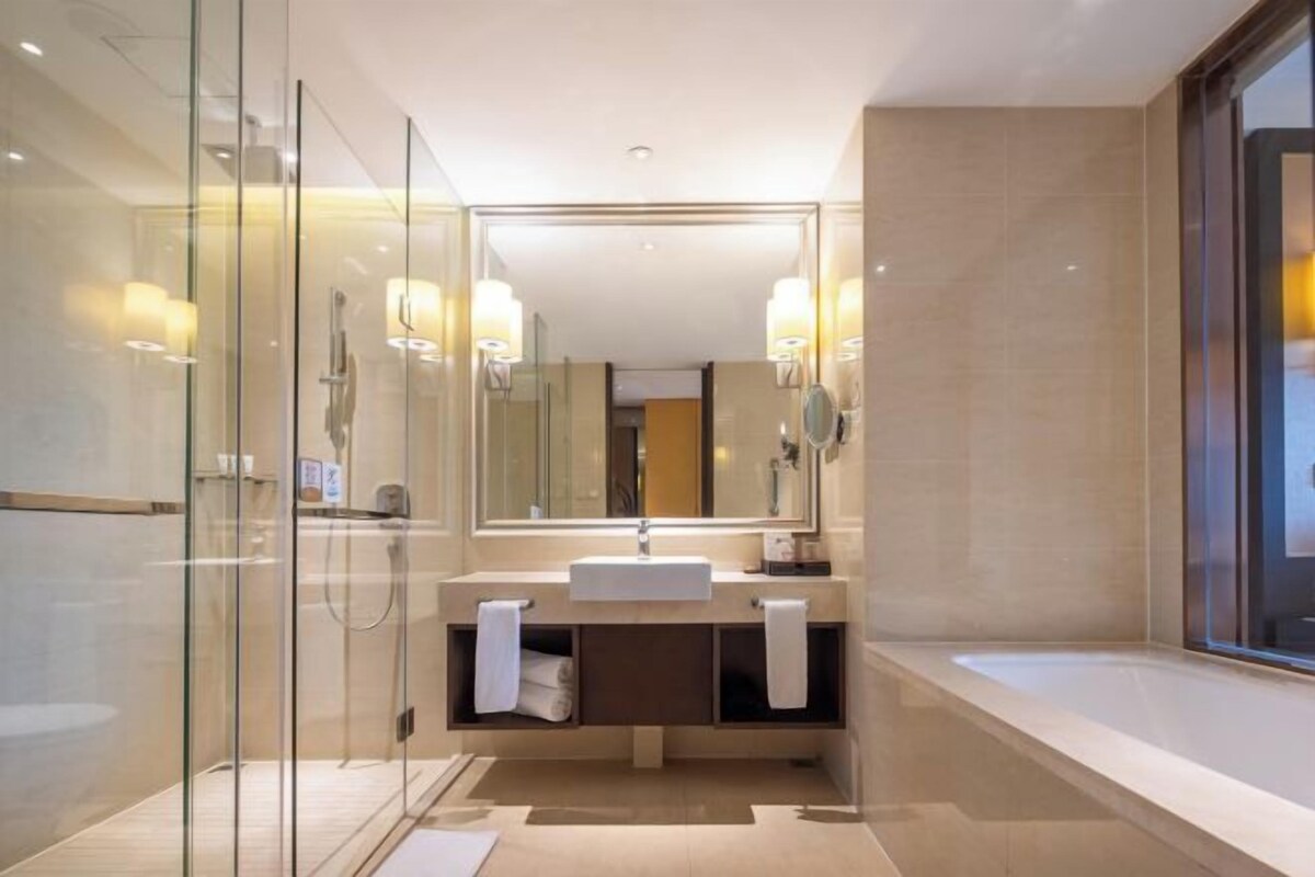 Une salle de bain moderne dotée d’une douche à parois de verre, d’un grand miroir et d’un meuble-lavabo avec deux porte-serviettes.