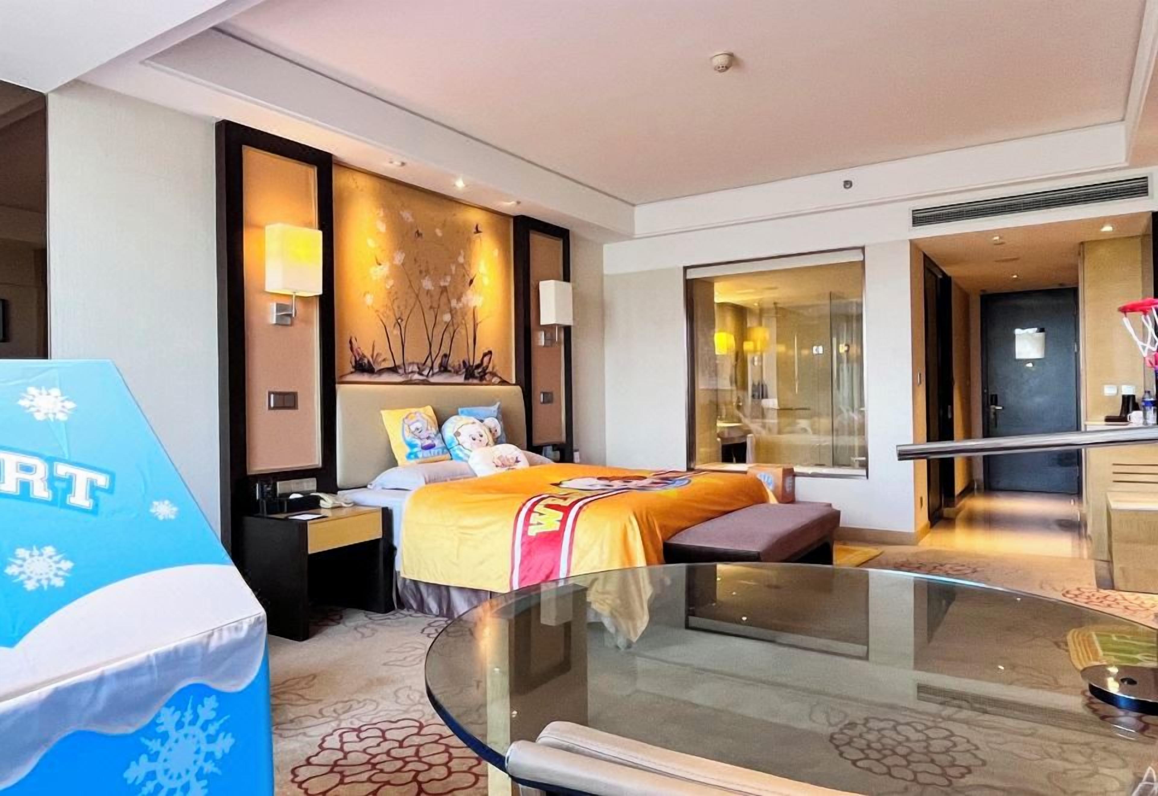 Une chambre d’hôtel avec un lit, des tables de chevet, une table en verre et une vue sur le couloir.
