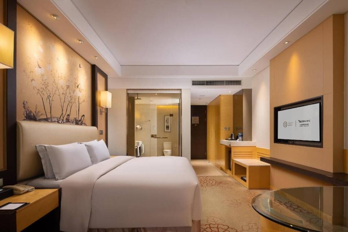 Een hotelkamer met een groot bed, een bureau met een lamp, een televisie en een badkamer door een open deur zichtbaar.