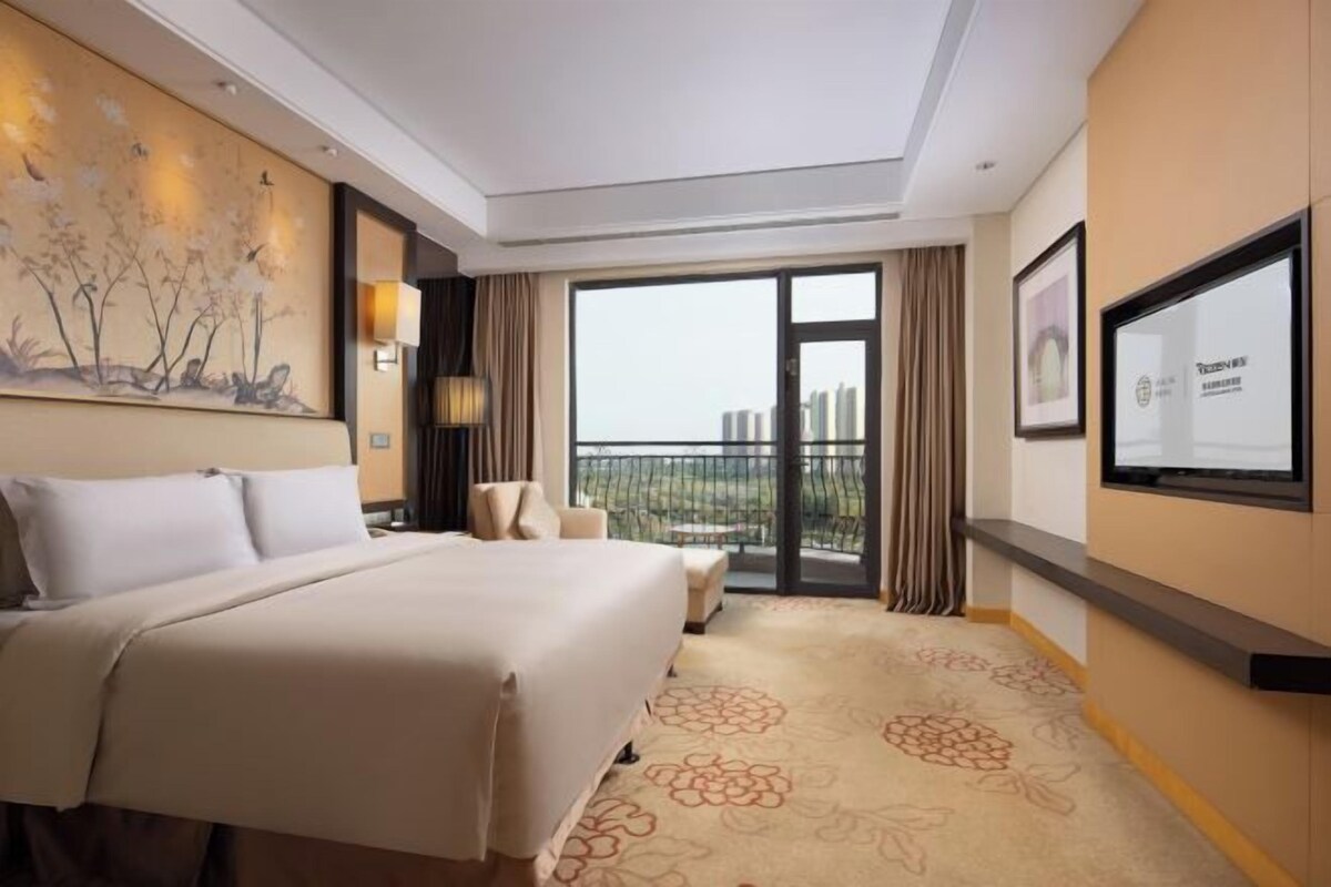 Une chambre d’hôtel avec un grand lit, un bureau, une chaise, une télévision et un balcon offrant une vue sur la ville.