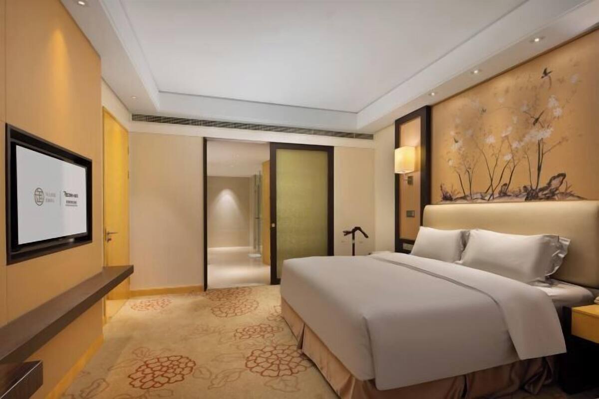 Een hotelkamer met een bed, een televisie, een schilderij en een deur die naar een andere kamer leidt.