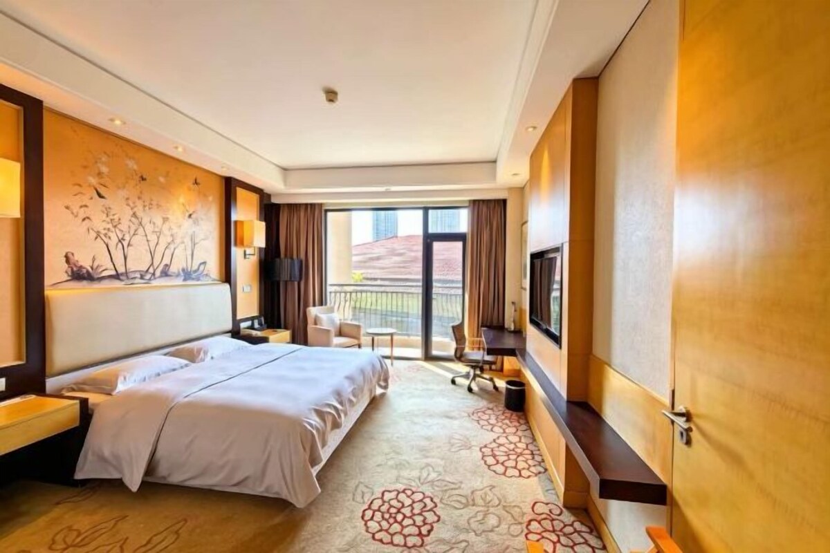 Une chambre d’hôtel équipée d’un lit, d’un bureau, d’une chaise, d’une télévision et d’un balcon avec vue.