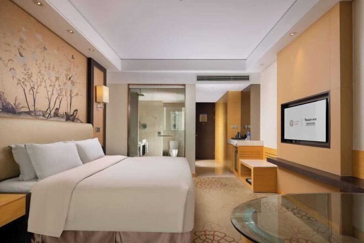 Een hotelkamer met een groot bed, een glazen tafel, een televisie en een schilderij aan de muur.