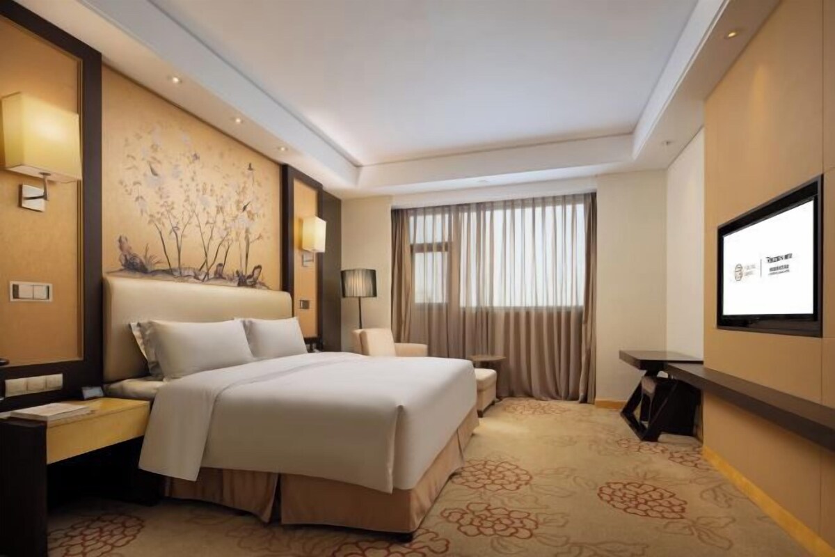 A hotel room with a bed, a desk, a chair, a TV, and a window with curtains.