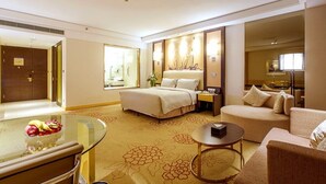 A hotel room with a bed, a sitting area with a sofa and armchair, a glass table with fruit, and a small round table. - Yuluxe Hotel Taizhou (Taizhou)
