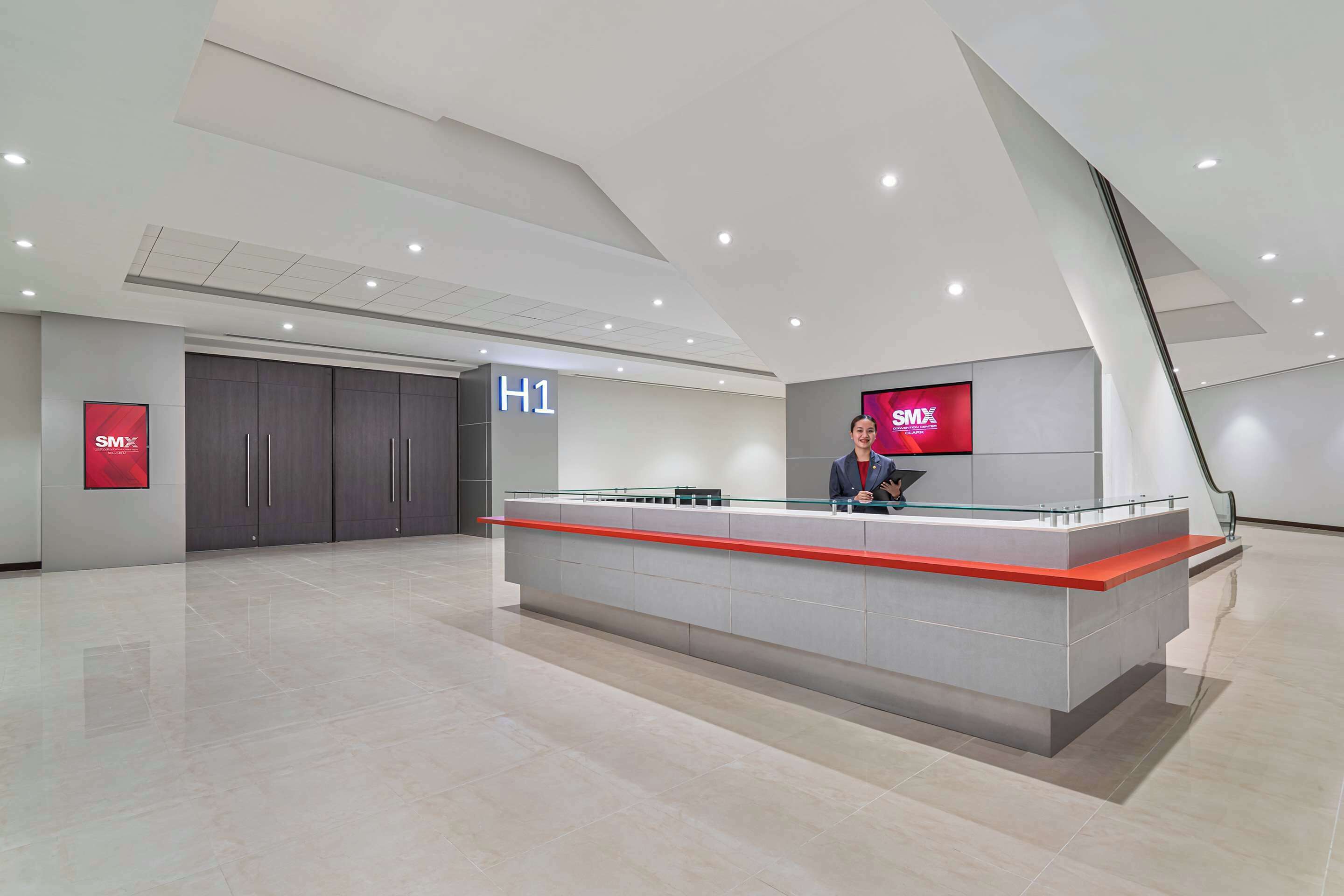 A modern hotel reception area with a glass counter, a digital display, and a sign indicating the hotel name.