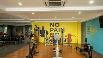 A gym with various exercise equipment, a wall with motivational text, and a wooden floor.