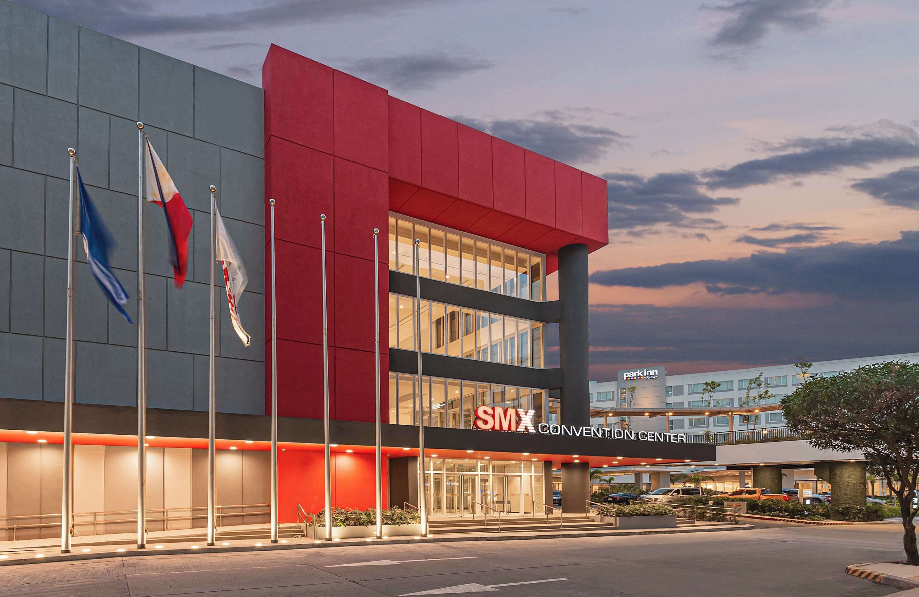A modern building with a prominent red facade, multiple flags, and a sign for 'SMX Convention Center'.