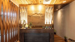 Un comptoir d’accueil avec un panneau en bois en arrière-plan, une enseigne indiquant « The Mandara Spa », et une rangée de produits de toilette en petits flacons.