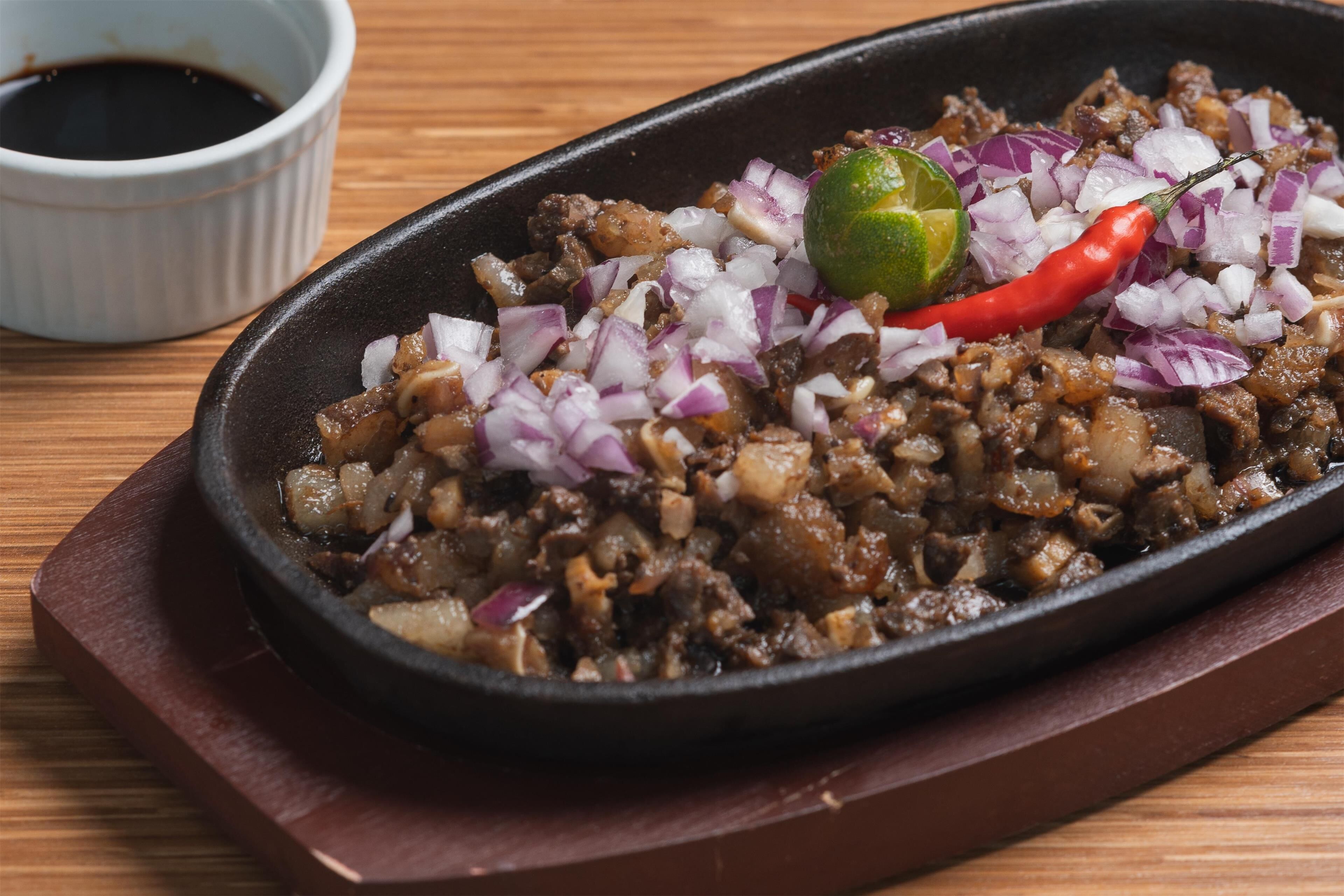 A dish with diced onions, a lime, and a red chili pepper on a black skillet.