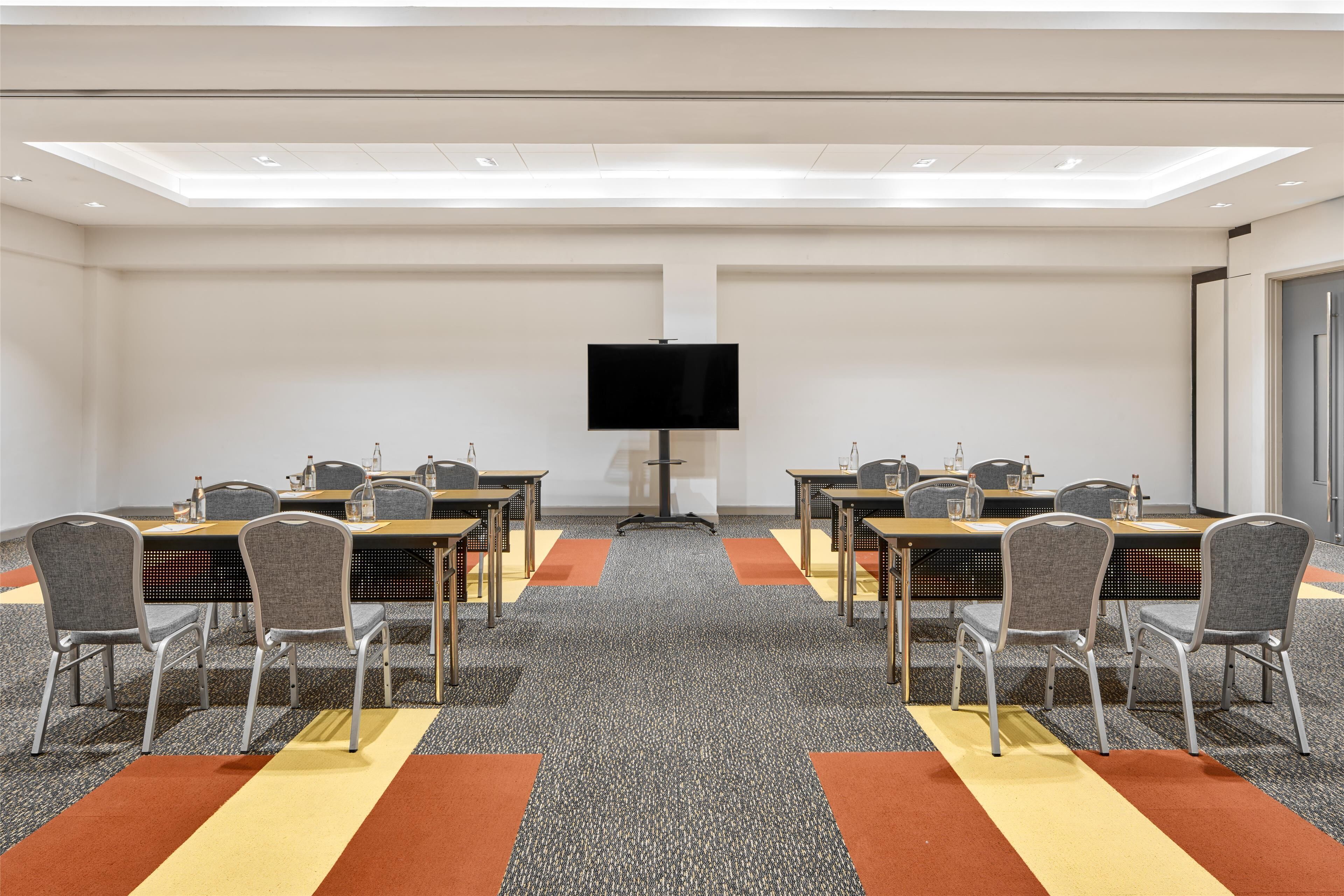 A conference room with a flat-screen TV, six tables with chairs, and a carpeted floor.