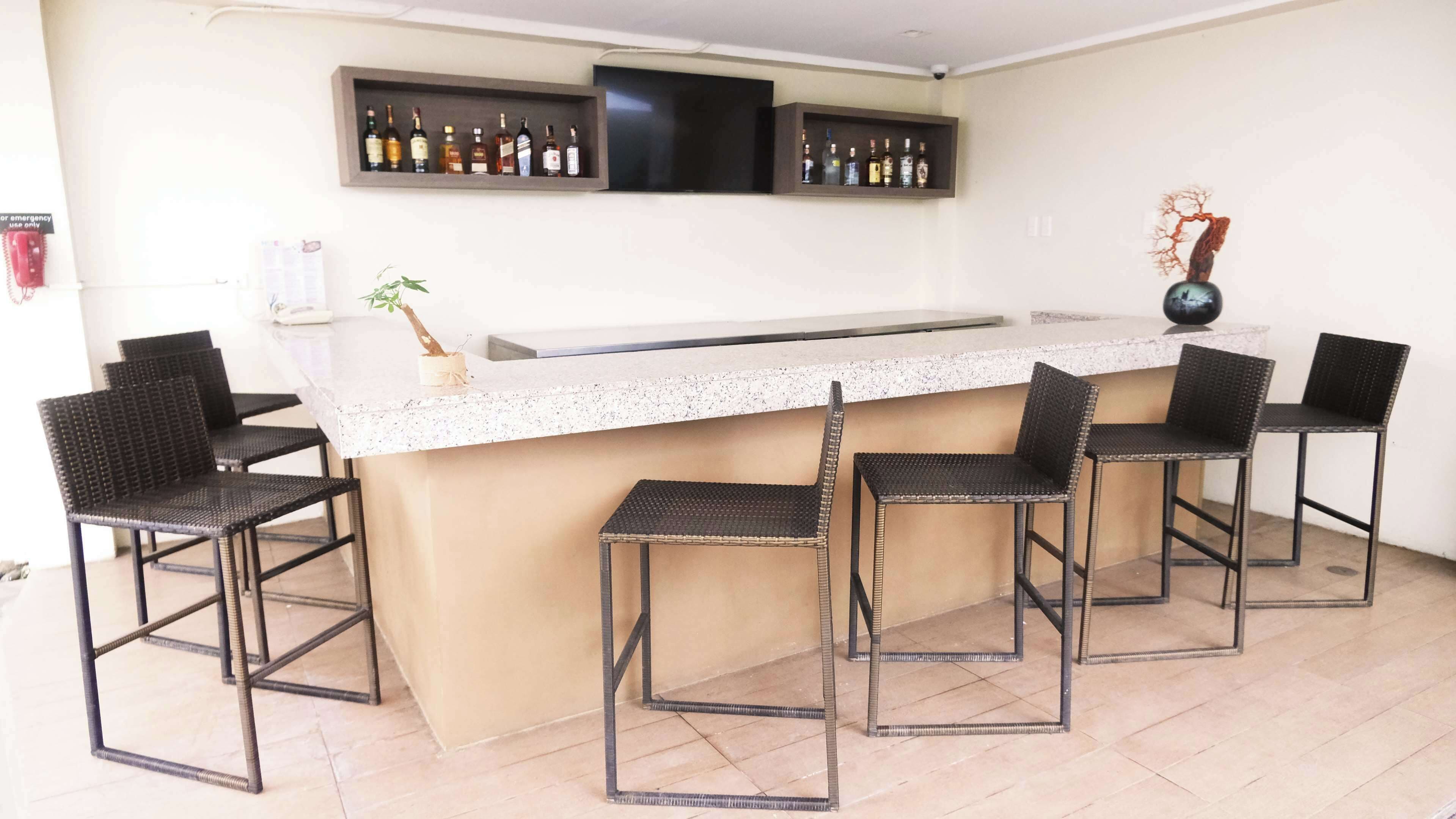 A bar area with a white countertop, four wicker chairs, and shelves with liquor bottles.