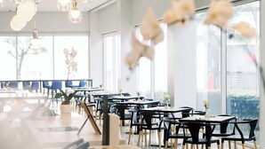Un espace de restauration moderne avec des chaises et des tables noires, de grandes fenêtres et des luminaires suspendus.