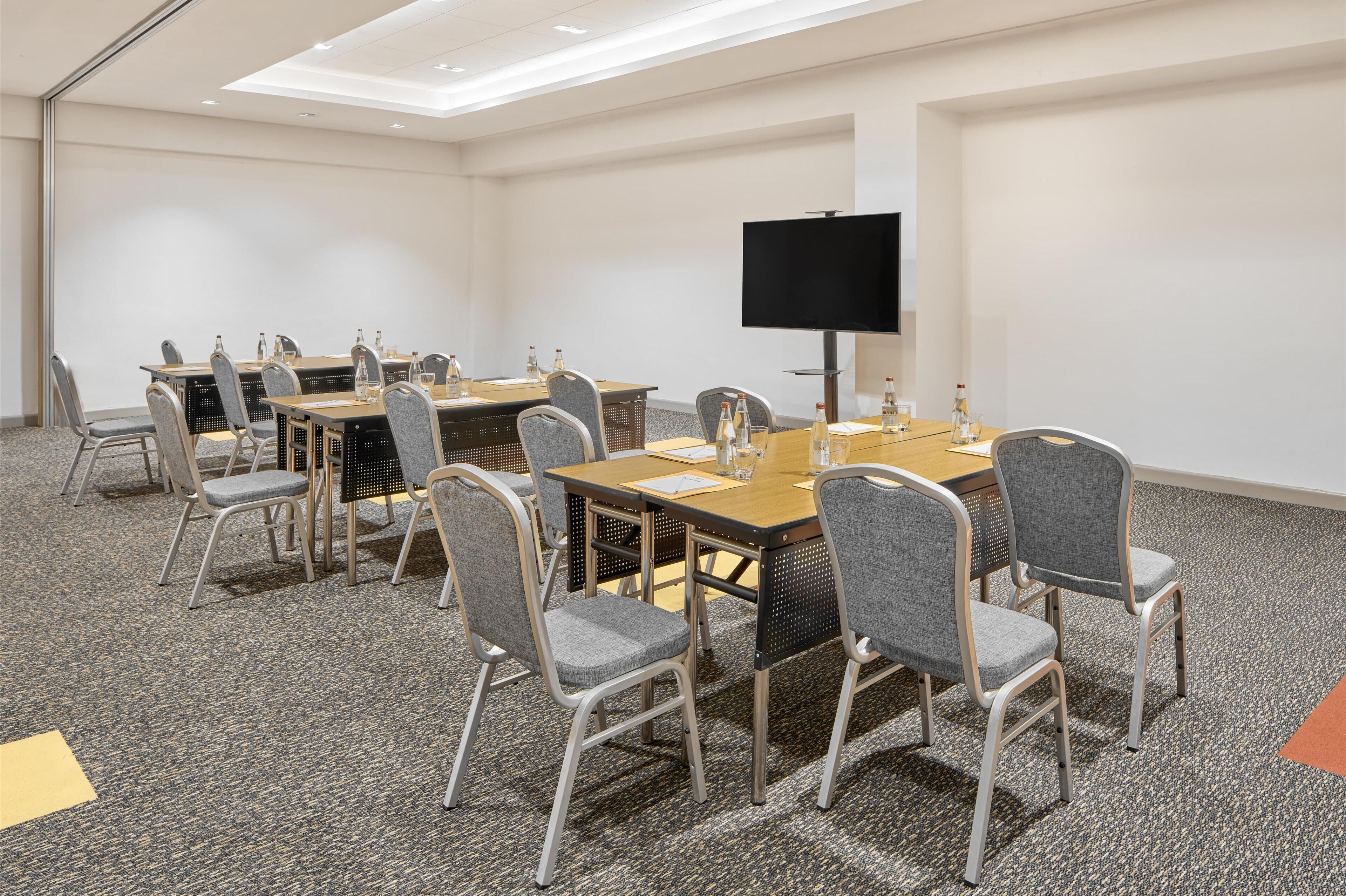A conference room with a large table, chairs, a flat-screen TV, and a carpeted floor.