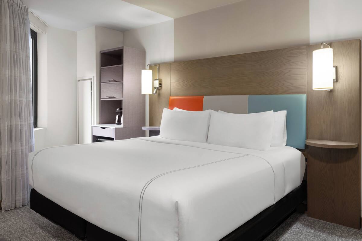 A hotel room with a large bed, a nightstand, a desk, and a wardrobe.