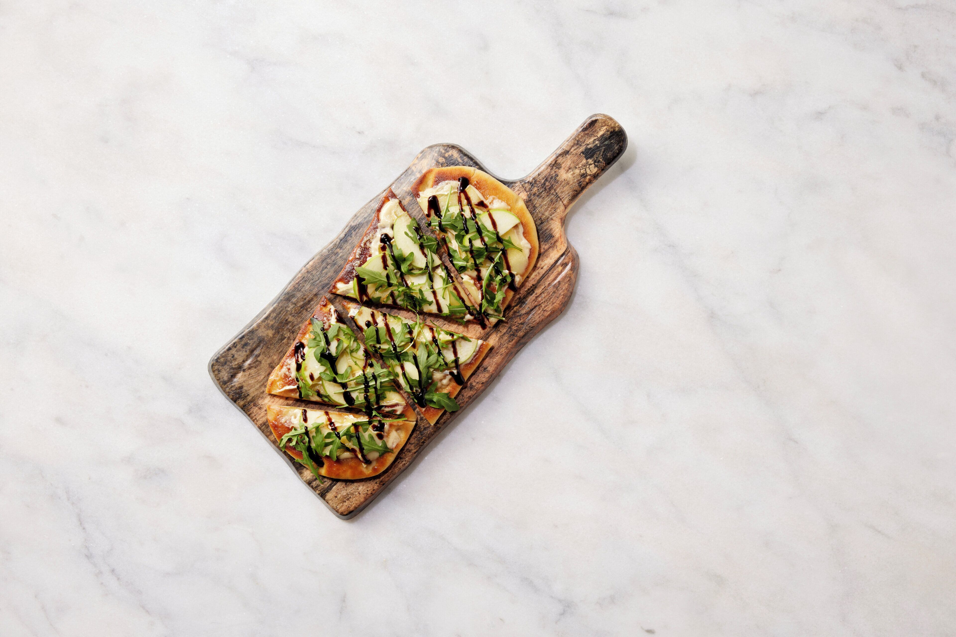 A wooden serving board with a rectangular dish containing sliced apples and greens, drizzled with a dark sauce.