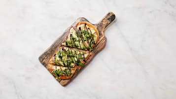 A wooden serving board with a rectangular dish containing sliced apples and greens, drizzled with a dark sauce.
