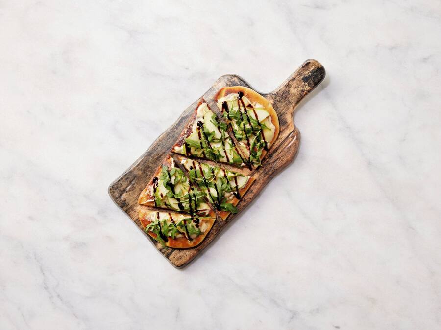A wooden serving board with a rectangular dish containing sliced apples and greens, drizzled with a dark sauce.