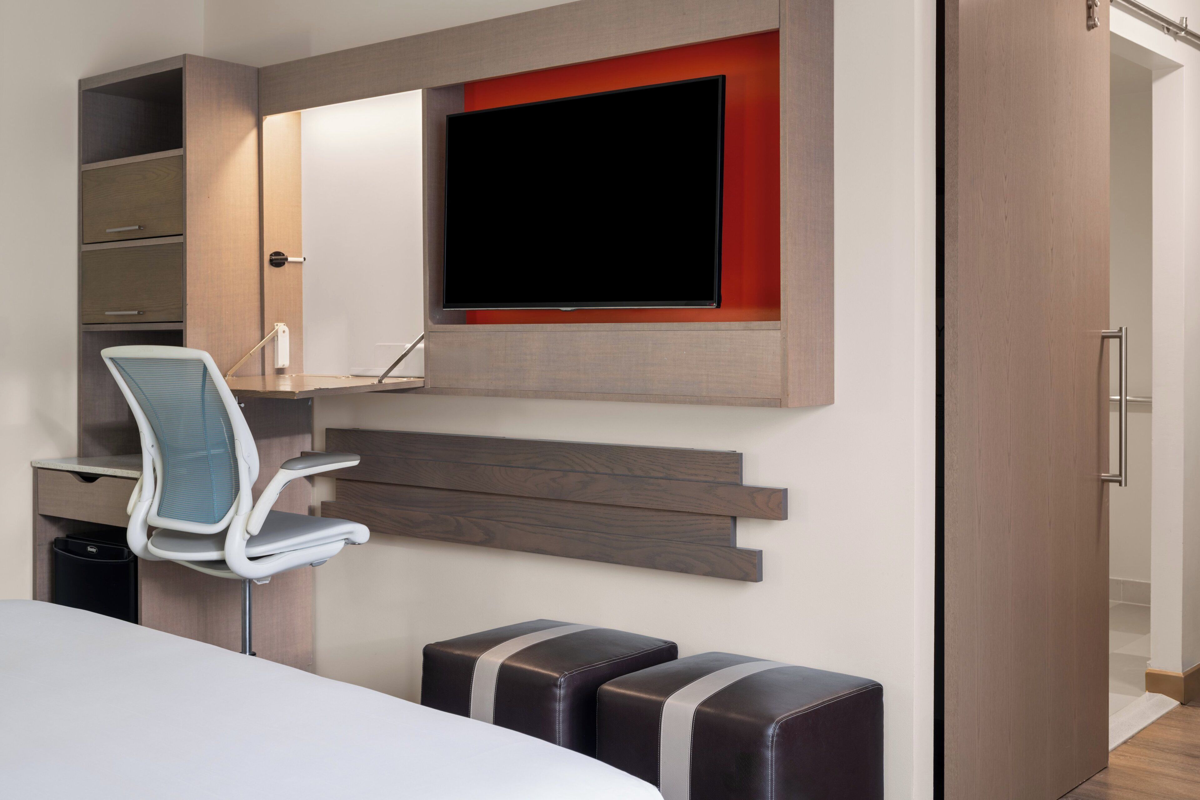 Habitació d'hotel moderna amb llit, escriptori amb cadira, televisió penjada a la paret i armari.