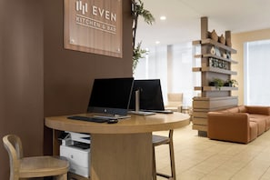 A modern kitchen and bar area with a wooden table, two HP desktop computers, a printer, a brown leather sofa, and a shelving unit with decorative items.