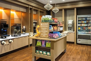 A self-service kiosk with snacks, a coffee machine, and a refrigerated beverage dispenser in a hotel setting.