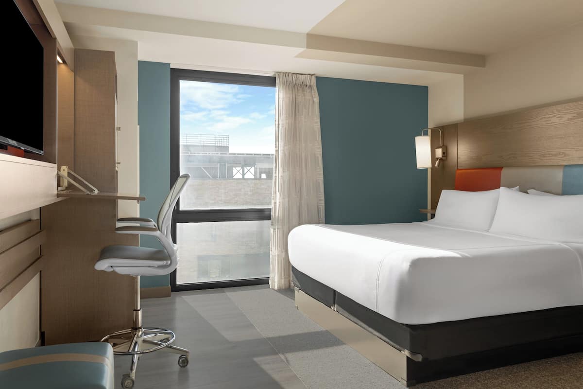 A hotel room with a bed, desk, chair, and a view of the outside.