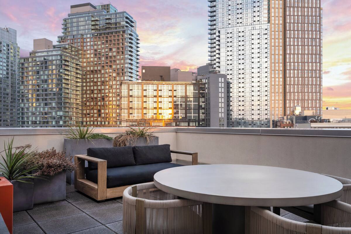 A rooftop terrace with a round table, a sofa, and potted plants.