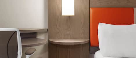 Une chambre d’hôtel équipée d’un lit, d’un bureau, d’une chaise et d’un luminaire fixé au mur.
