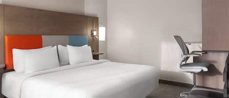 A hotel room with a large bed, a desk with a chair, and a wall-mounted light.