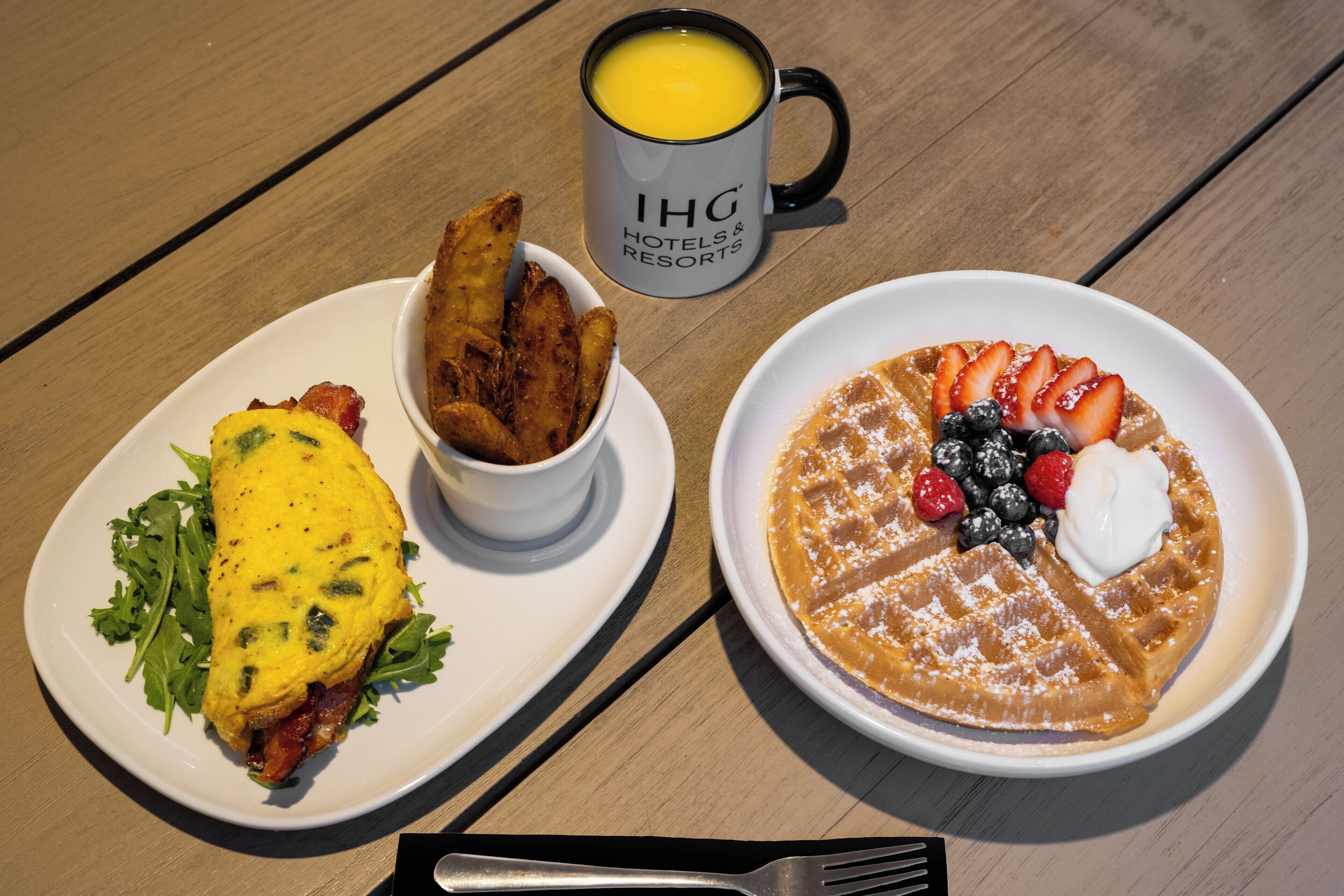 A breakfast plate with an omelet, a bowl of fries, and a waffle with berries and whipped cream.