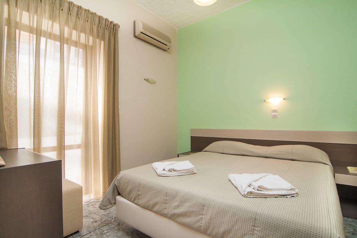 A hotel room with a bed, a desk, and a window with curtains.