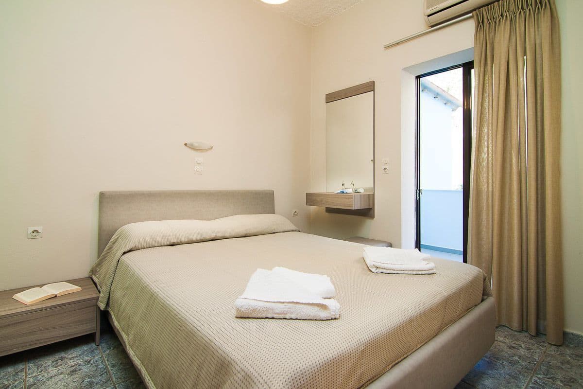 A hotel room with a bed, a bedside table, a mirror, a window with curtains, and a balcony.
