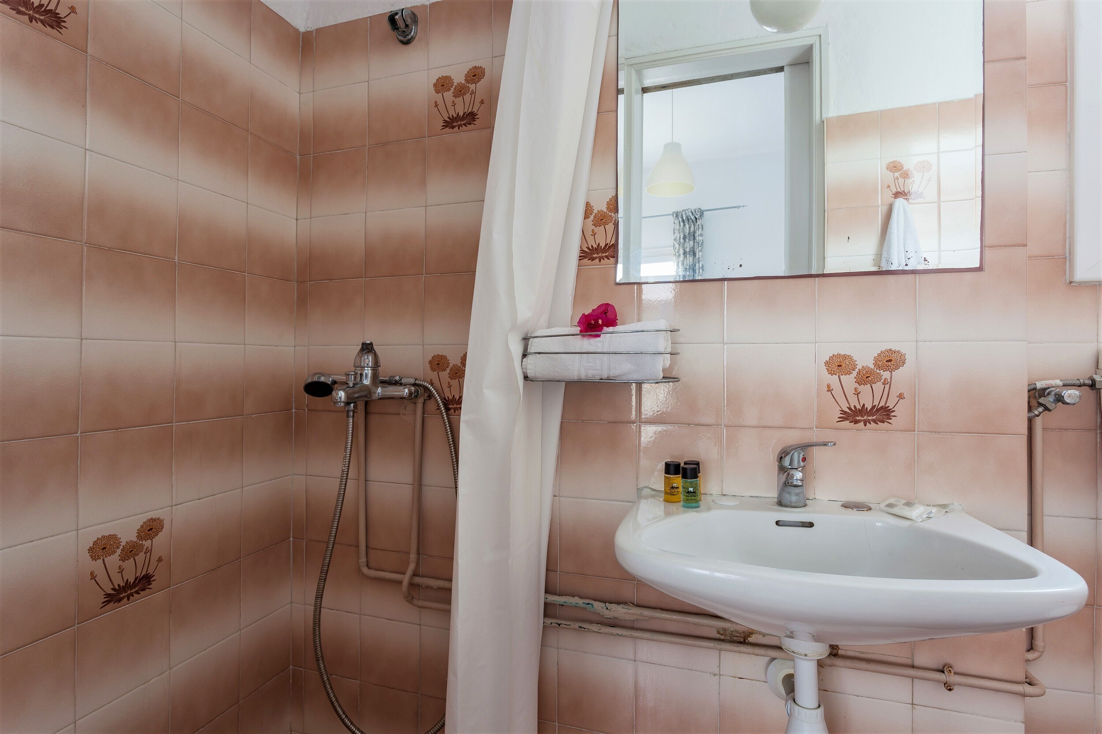 Un bagno con piastrelle rosa, un lavandino bianco, uno specchio e una zona doccia.