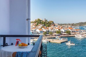 A balcony with a table, a bowl of fruit, and a view of a coastal town with boats and buildings. - Argo (Skiathos)