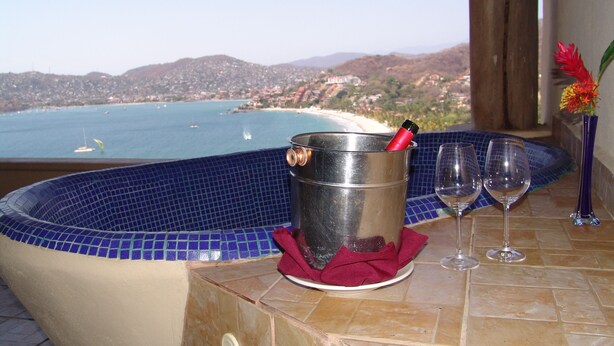 Un bain à remous avec vue sur la plage et les montagnes, un seau contenant une bouteille et deux verres à vin, le tout posé sur une surface carrelée.