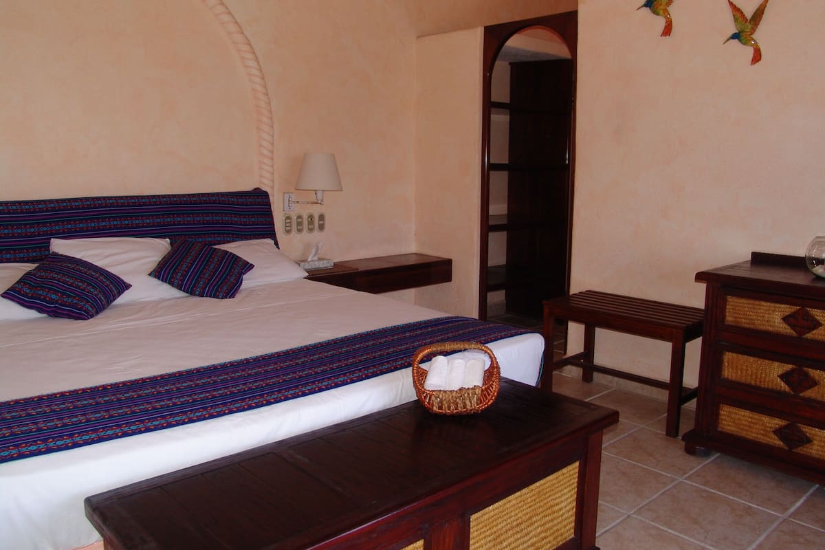 Une chambre d’hôtel avec un grand lit, une table de chevet, une commode, une lampe et deux décorations murales représentant des oiseaux.
