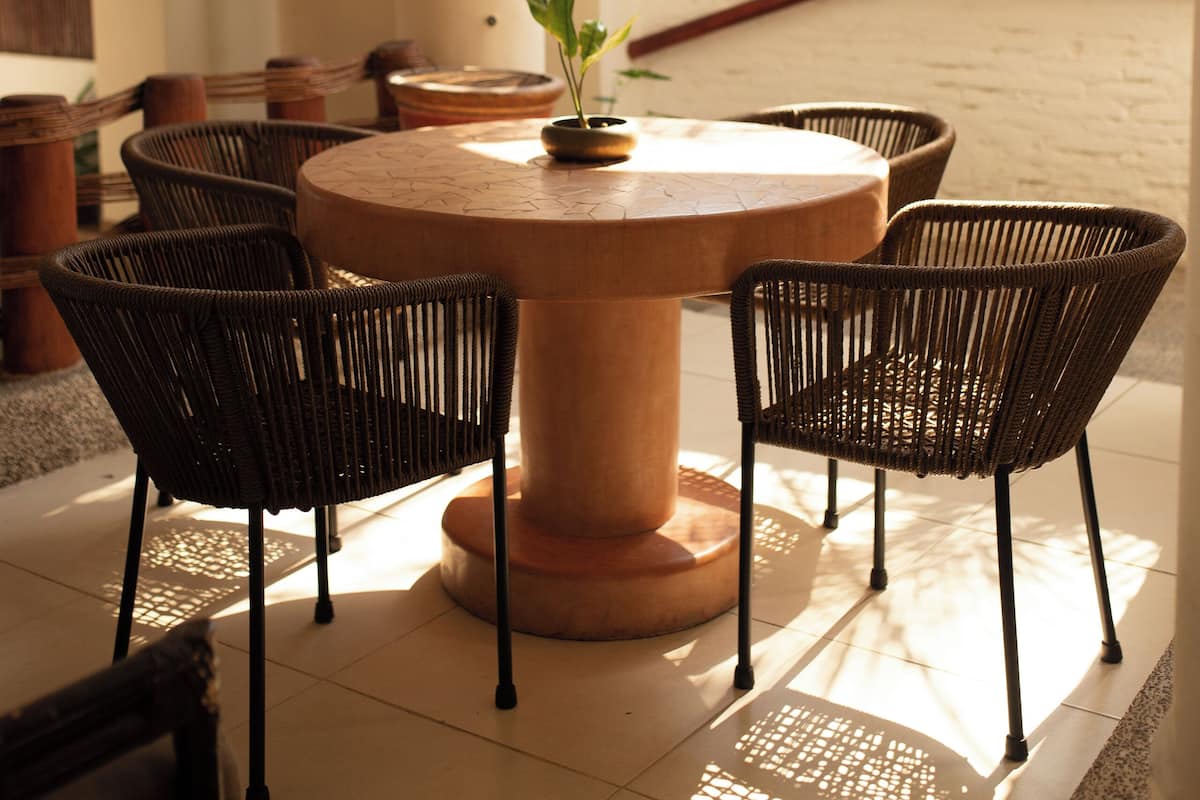 A round table with chairs, a potted plant, and a white brick wall.