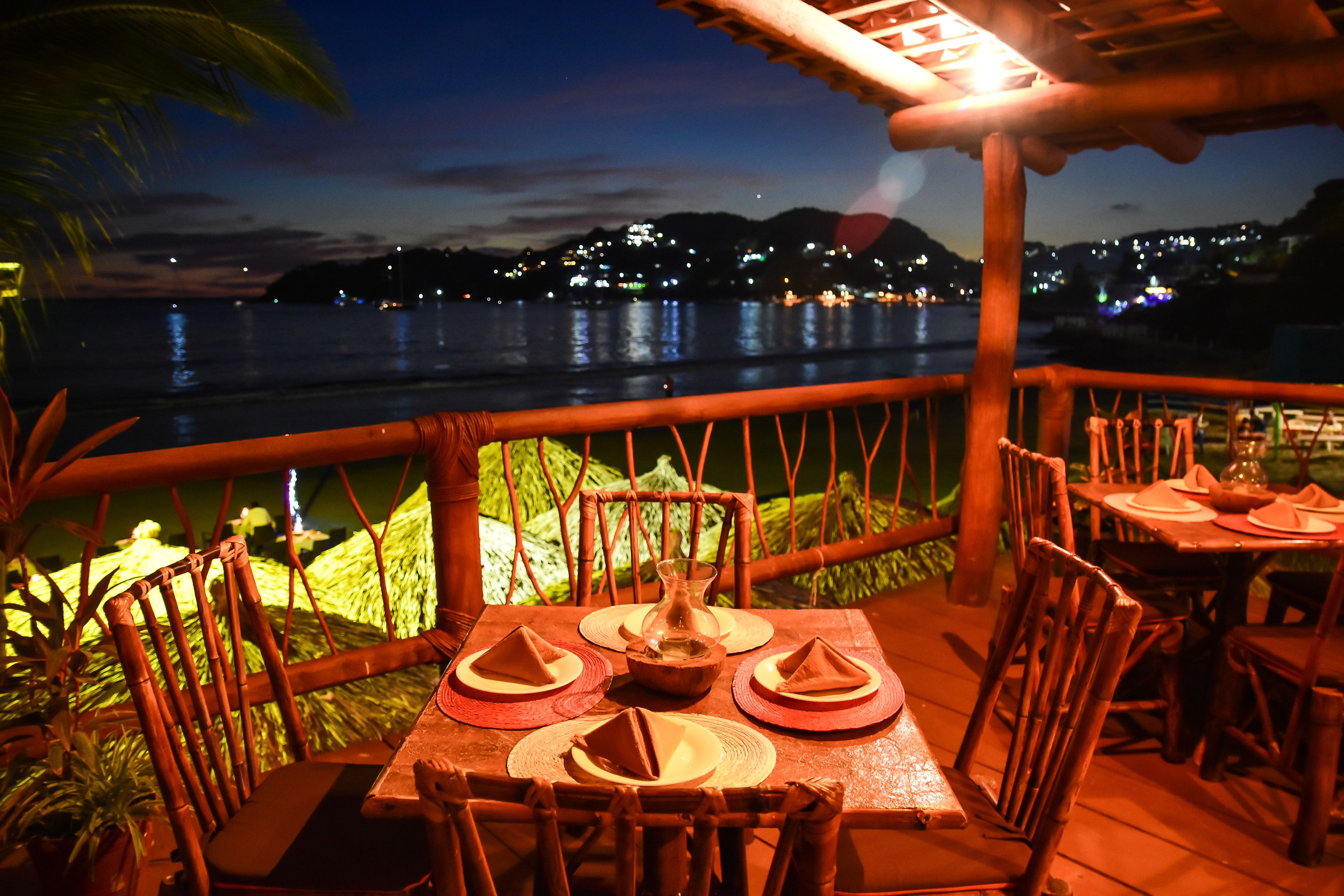 An outdoor dining area with wooden furniture and a view of the water at night.