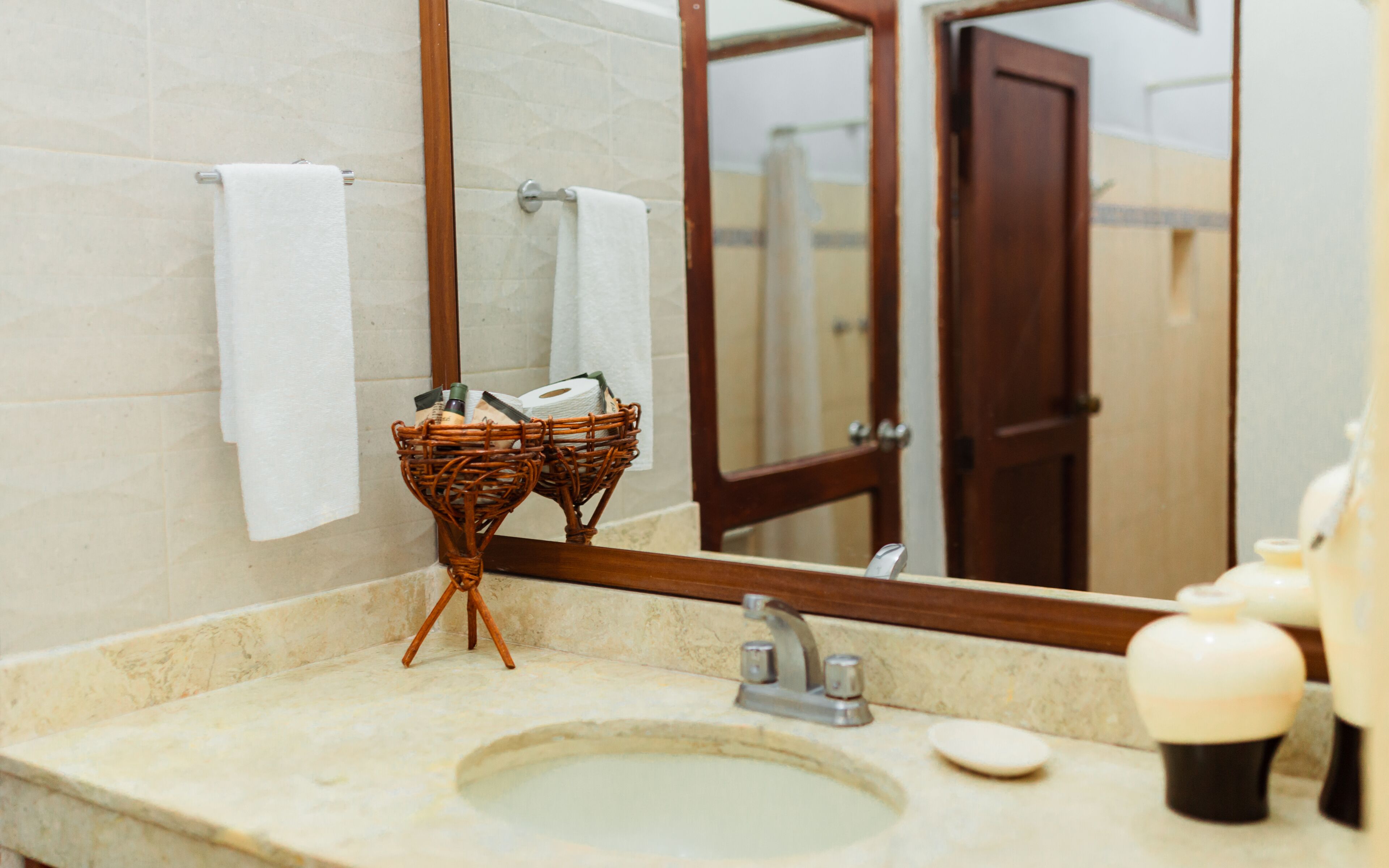A bathroom with a marble sink, a mirror, and a wicker basket holding toiletries.