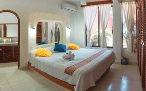 A hotel room with a large bed, a wooden dresser, a mirror, and a window with curtains. - Arena Suites (Zihuatanejo)