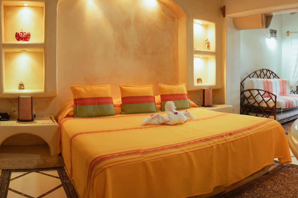 A hotel room with a large bed, multiple pillows, bedside lamps, a small statue, and a decorative rug.
