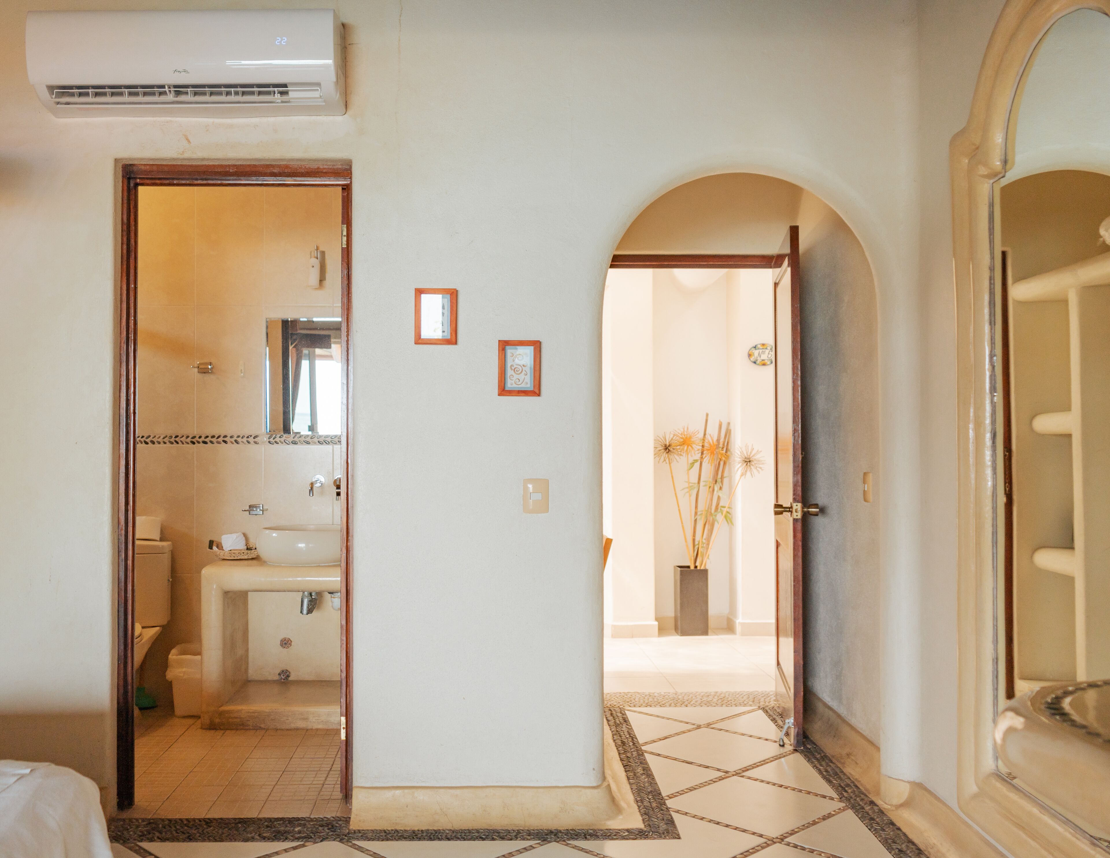 Pasillo de hotel con un baño, piso de baldosas y una puerta que da a otra habitación.
