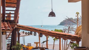 Un espace de restauration en plein air offrant une vue sur la mer, avec une table ronde, des chaises en osier et des lanternes suspendues.