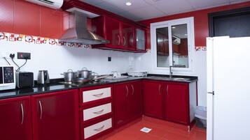 Una cocina con armarios rojos, una campana extractora de acero inoxidable, un microondas, un tostador y un fregadero.