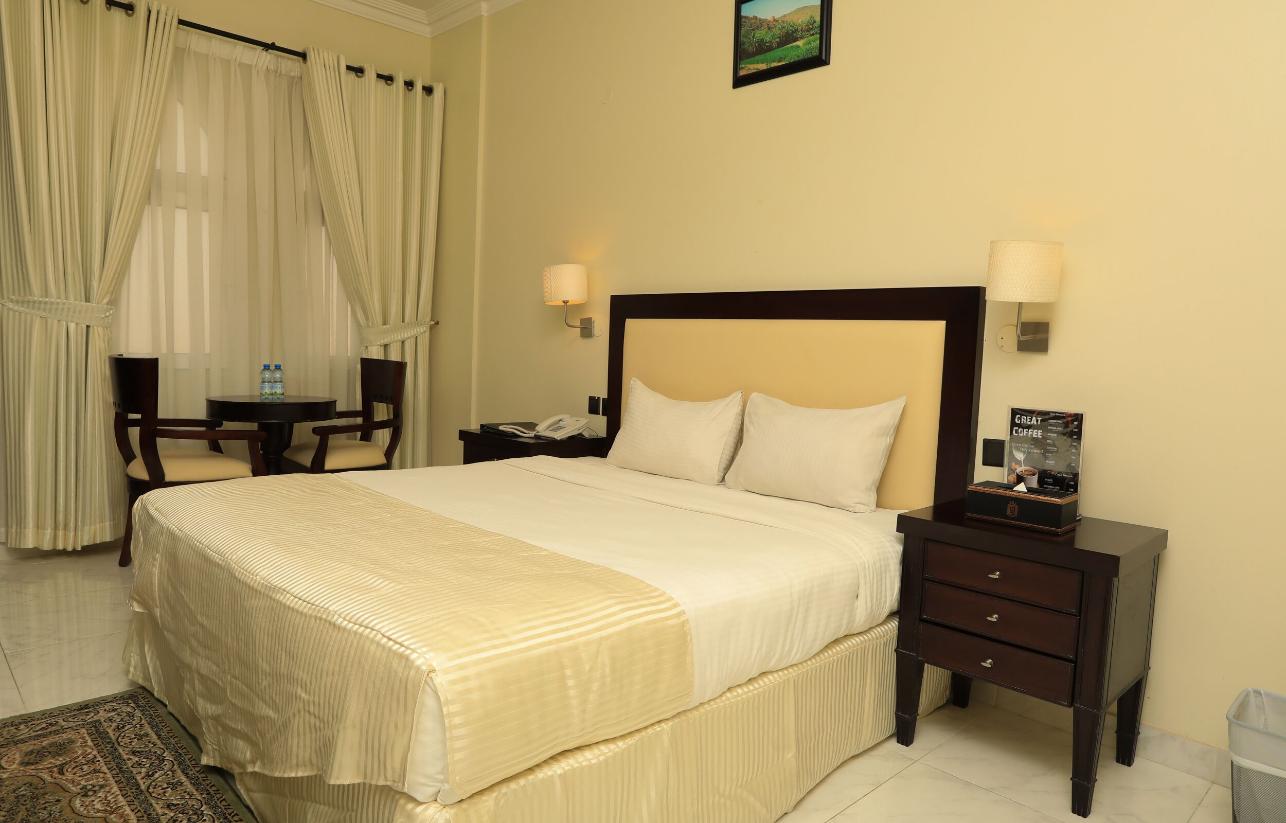 A hotel room with a bed, bedside tables, a lamp, a chair, a desk, and a picture frame.