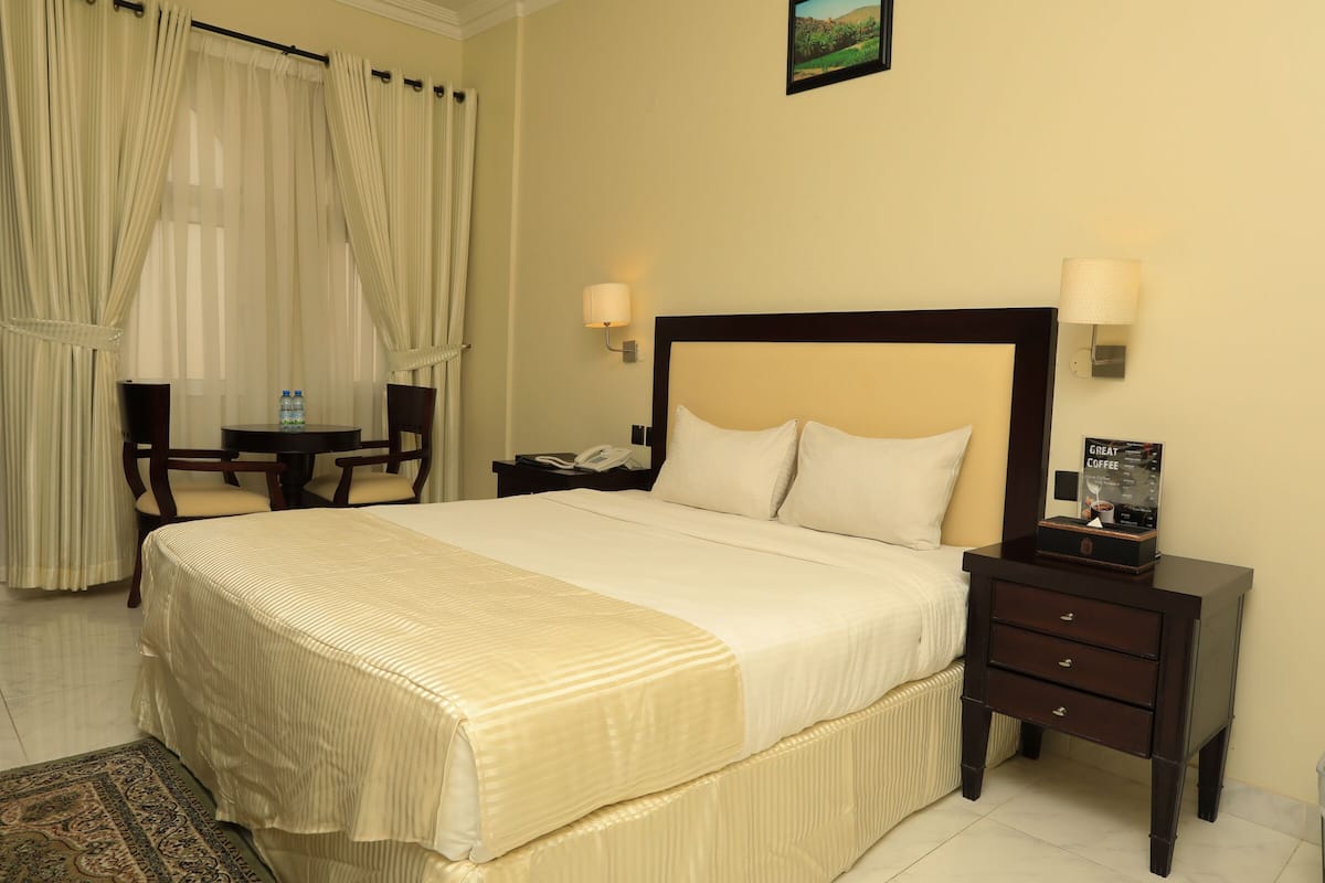 A hotel room with a bed, bedside tables, a lamp, a chair, a desk, and a picture frame.