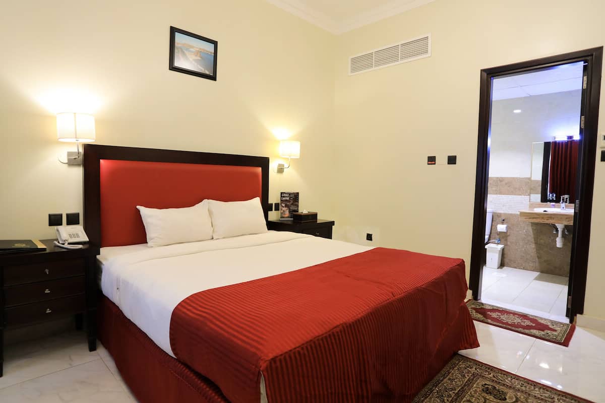 A hotel room with a bed, nightstands, a phone, and a bathroom visible through an open door.
